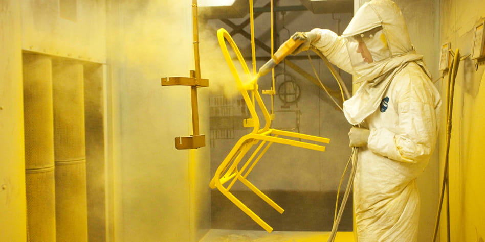 A factory employee powder coating a banquet chair.