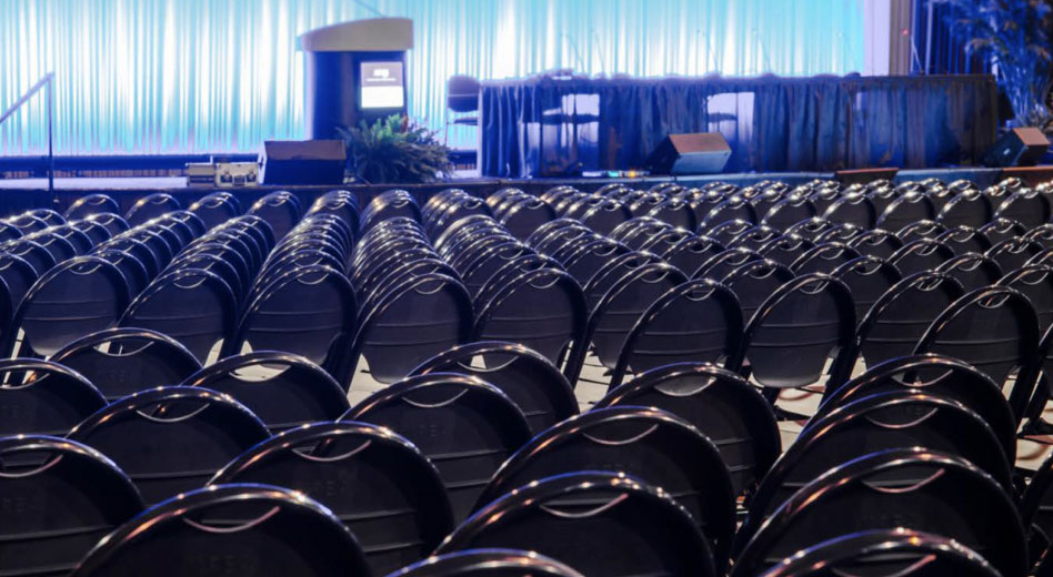 Filas de sillas MityLite en una sala espaciosa con un escenario preparado para un evento.