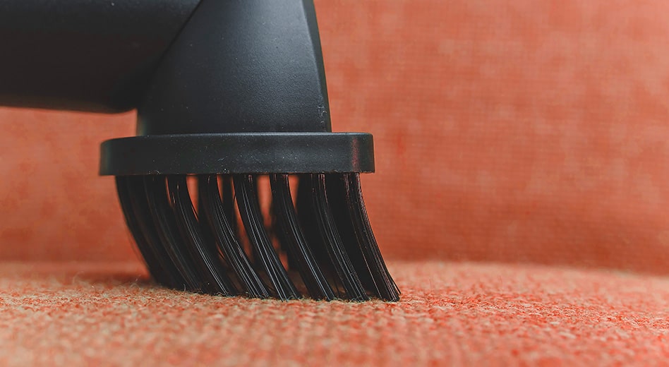 Close-up of a bristled vacuum hose on an orange-colored upholstery