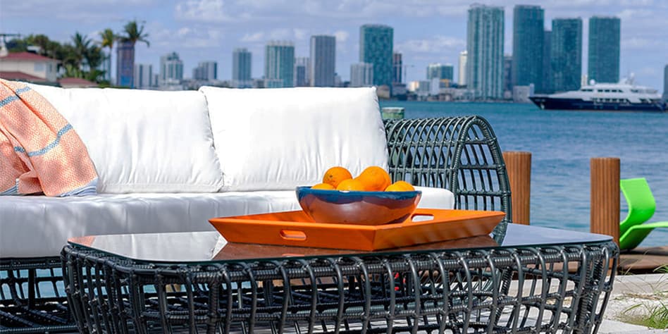 black outdoor furniture with white cushions on a waterside patio with a cityscape in the background