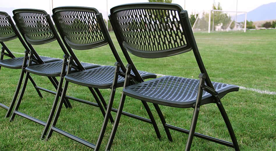 plastic folding chairs with metal frames lined up along the sidelines of a football field