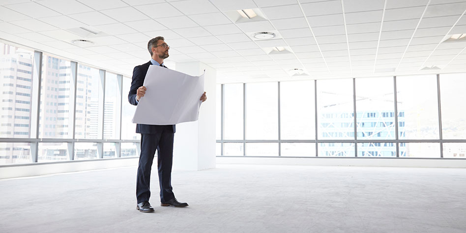 Man considering plans as he stands in a large, empty space