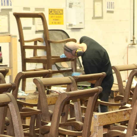 A man is doing a final sanding on the wooden chair frame