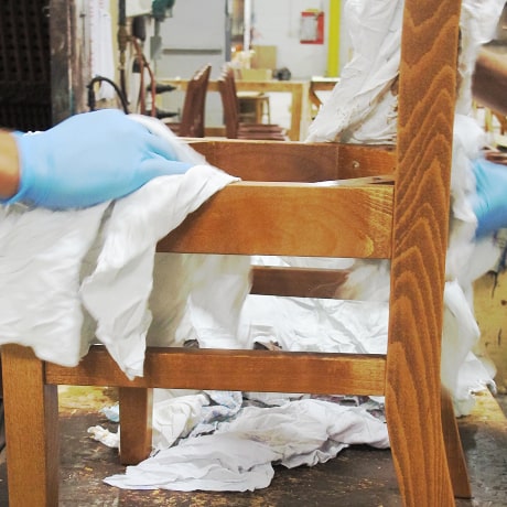 A wooden chair frame is hand-wiped with a cloth after being stained