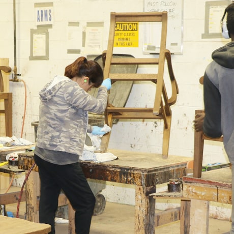 A woman is sanding a wooden chair frame after sealant has been applied