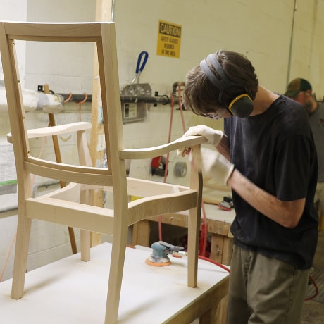 Man sanding a wooden chair frame in a factory