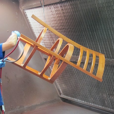 A wooden chair frame is being sprayed with sealant after staining process