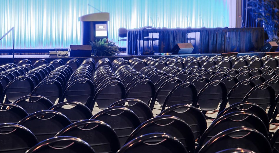 Une photo de centaines de chaises pliantes face à une scène dans une salle de conférence