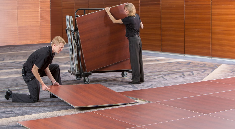 Two people assembling magnetic dance floor panels in a banquet hall