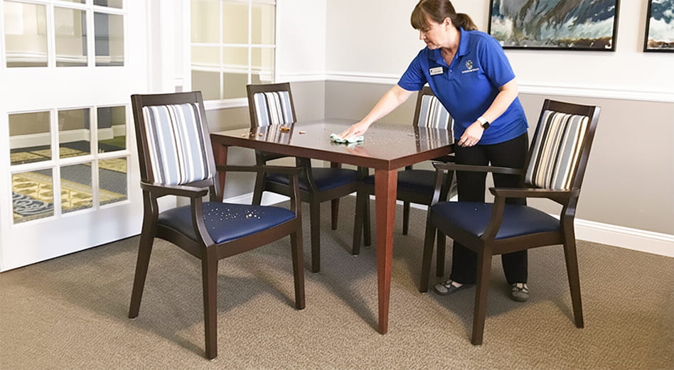 Staff member in a senior living facility cleaning off a table and chairs